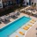 Apartments in Charlotte, NC, for Rent - Amaze at Noda - Swimming Pool with Orange Submerged Lounge Seats, Blue Poolside Chairs, Covered Cabanas, Landscaped Plant Beds, and View of Outdoor Lounge Area.